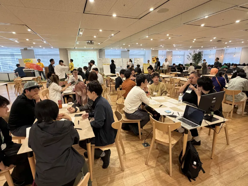 広い会場でテーブルごとに分かれてワークに取り組む大勢の参加者